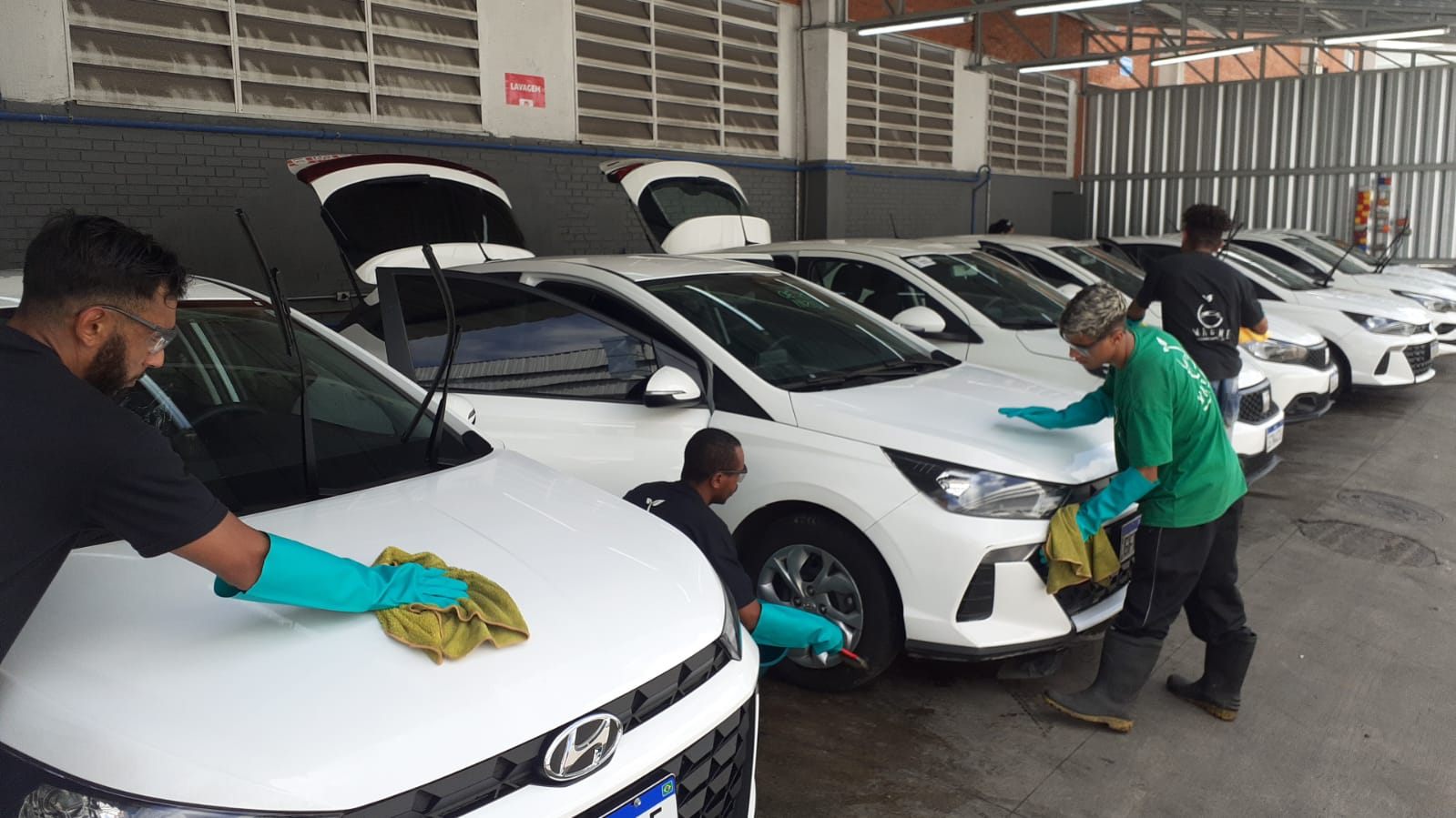 Três operadores Wash Me lavando uma frota de carros em pátio coberto de cliente